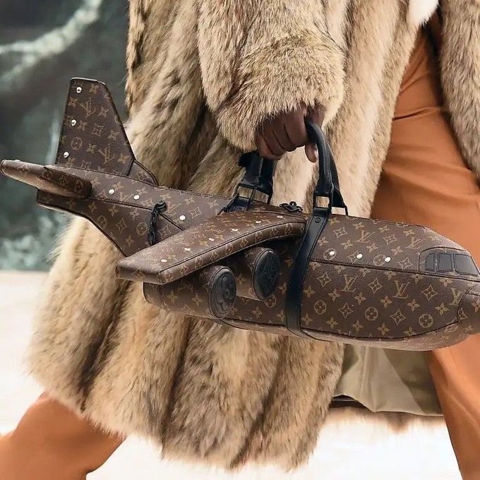 A person wearing a luxurious fur coat carries a Louis Vuitton airplane-shaped handbag featuring the iconic monogram pattern, with a brown leather handle and gold-tone hardware. The novelty bag showcases the recognizable LV logo throughout its design.