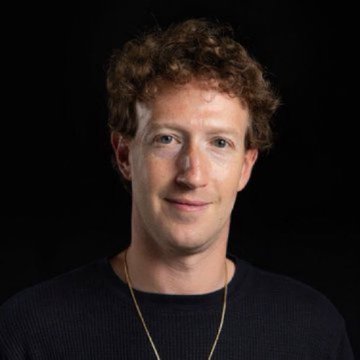 A portrait of a young man with curly brown hair wearing a dark sweater and a gold chain against a black background.