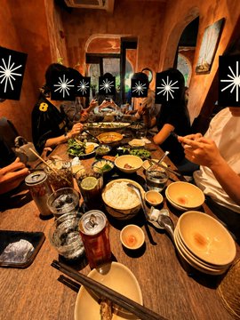 A group of people gather around a long wooden table filled with shared dishes of rice, noodles, and vegetables in bowls, enjoying a communal Vietnamese meal together. Several faces in the photo have been covered with black starburst stickers for privacy, reflecting the offline gathering mentioned in the post welcoming @0xsexybanana to Vietnam with the Axis Vietnam team.