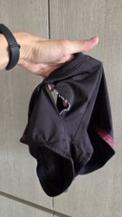 A hand holding up a pair of black athletic shorts with pink interior lining against a light-colored wall.