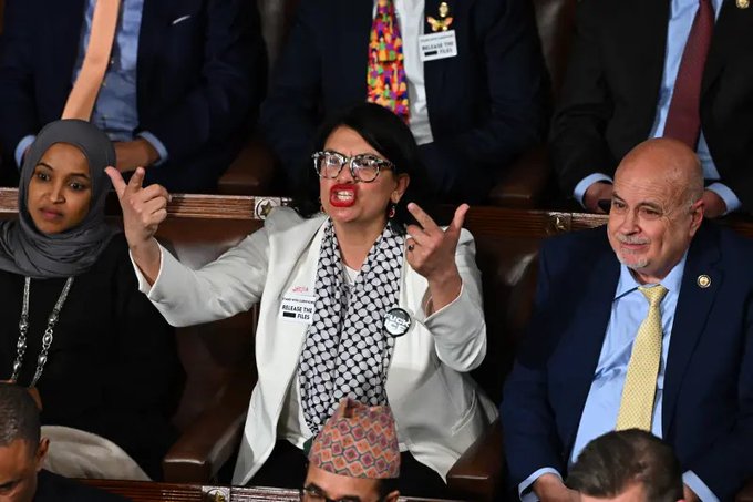 Representative Rashida Tlaib, wearing a white blazer and a scarf, gestures with her hands in the House of Representatives, where she voted against the CLARITY Act, despite her financial disclosures showing she holds Bitcoin and Ethereum.