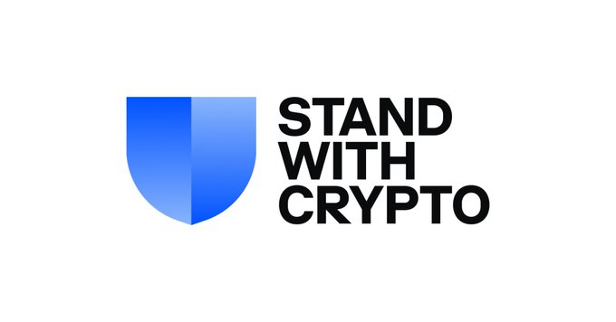The image displays the "Stand With Crypto" logo, featuring a blue shield icon next to the organization's name in bold black text. This visual aligns with the post about the advocacy group's initiative to track lawmakers' votes on cryptocurrency legislation, specifically noting how it will mark senators who opposed the CLARITY Act on its scorecards before the November midterms.