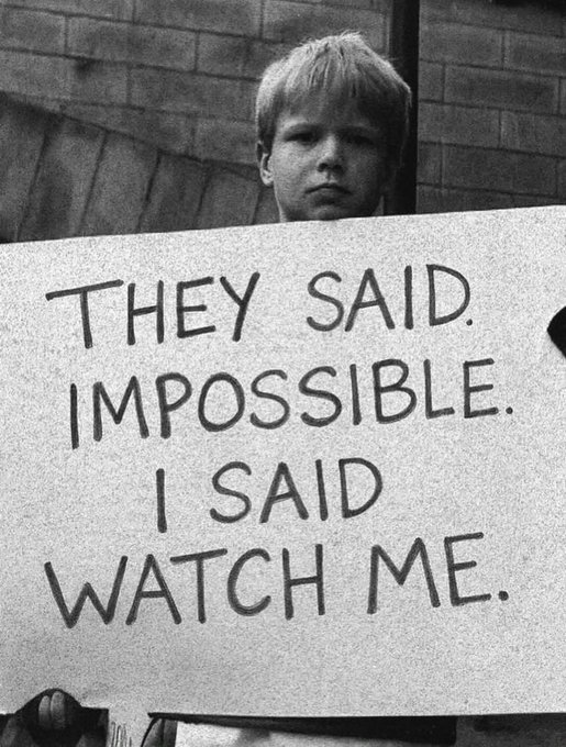 A black-and-white photo of a young boy holding a sign that reads 'THEY SAID IMPOSSIBLE. I SAID WATCH ME.'