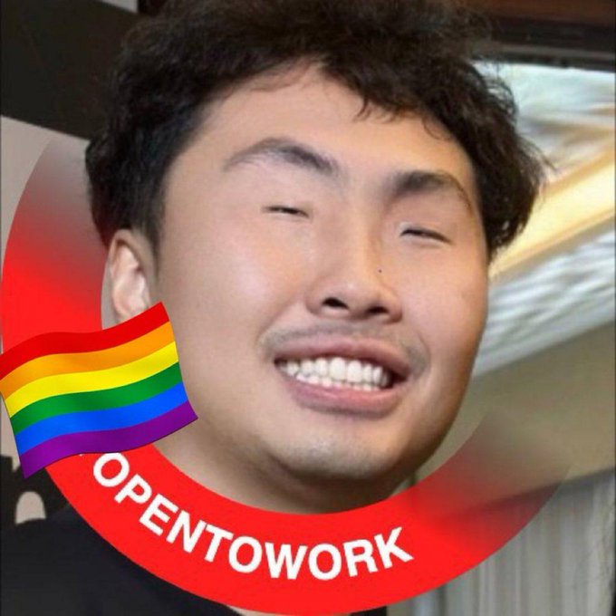 The image features a man with black hair wearing a black shirt, who appears to be smiling at the camera. There are two rainbow flags present in the photo, one located above his head and another below his chin. The text "openwork" is written on the bottom of the image.