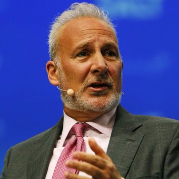 Peter Schiff, wearing a gray suit and pink tie, speaks into a headset microphone while gesturing with his hand, captured during an on-stage appearance that aligns with his commentary warning that AI—not Bitcoin—will dominate future investment trends.