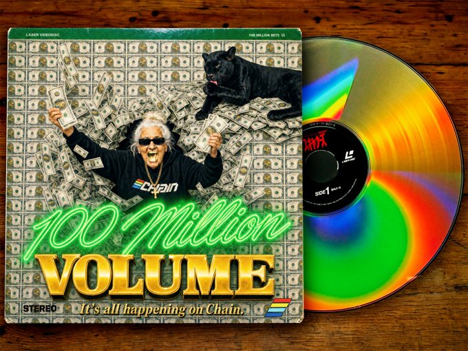 A LaserDisc cover for '100 Million Volume' featuring a man surrounded by dollar bills with a black panther, alongside a physical disc showing rainbow reflections, with text 'It's all happening on Chain.'