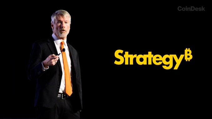 Michael Saylor, Executive Chairman of Strategy, stands in a dark suit with an orange tie on stage beside the yellow "Strategy₿" logo, as the CoinDesk watermark appears in the upper right. The image ties to the post about Saylor's weekly chart signaling another potential $BTC purchase by the company he leads.