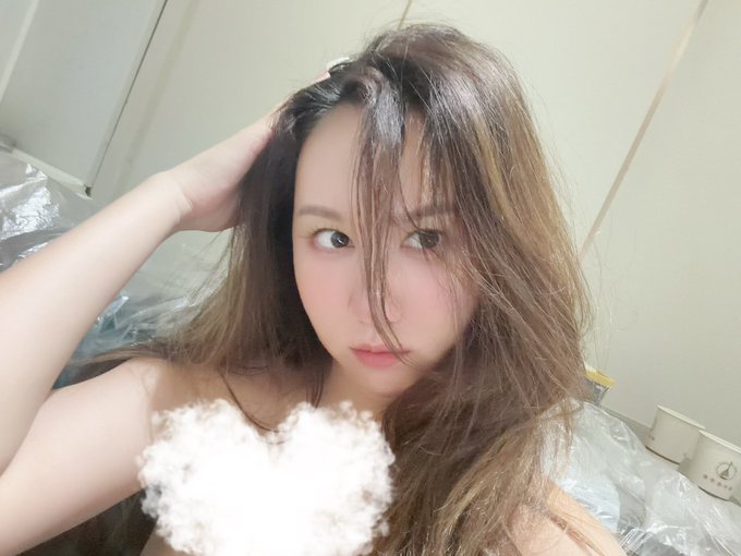 A young woman with long brown hair poses in a bathroom setting, appearing to be fresh from a bath as she runs her fingers through her still-damp hair. The image illustrates the post's mention of visiting the bathhouse, capturing a relatable post-bath selfie moment.