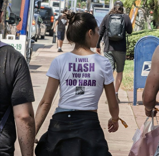 A woman walks on a sidewalk wearing a white t-shirt with purple text reading 'I WILL FLASH YOU FOR 100 HBAR' and a small graphic below it.