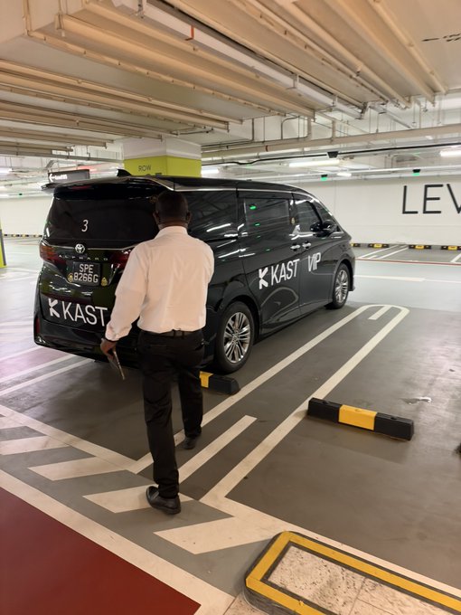 A man in a white shirt walks toward a black van branded with 'KAST' and 'VP' logos in an underground parking garage.