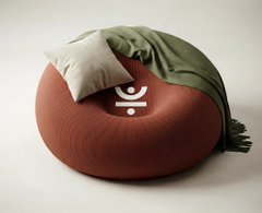 The image features a brown circular floor cushion with a white pillow and green throw blanket arranged on top, forming a cozy, reclined figure that suggests a comfortable resting place. A Justlend DAO logo (a stylized human figure) is overlaid on the cushion, symbolically representing the platform's two reward streams—mining rewards and TRON DeFi Summer S2 incentives—as a place for users to "rest" on their earnings.