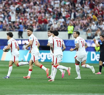 Turkish national football players in white jerseys with red trim, including numbers 13 and 8, celebrate together on the pitch while a large crowd cheers in the stadium background. The jubilant scene of teammates running together captures the excitement of a goal celebration, matching the post's teasingly understated "Eh... Ne diyelim..." ("Eh... What can we say...") tone.