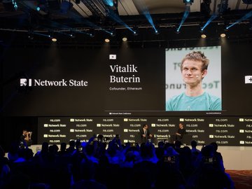 A stage at the Network State event displays a large screen featuring Vitalik Buterin, Co-founder of Ethereum, alongside his name and title, with branded backdrops visible behind an audience of attendees.
