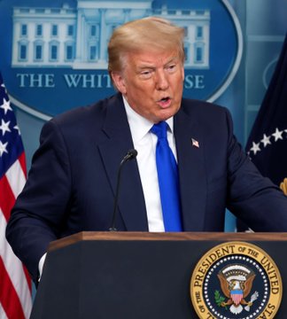 Former President Donald Trump stands at a White House podium bearing the Presidential Seal, with "THE WHITE HOUSE" displayed on the blue backdrop behind him and an American flag to his side. The image illustrates the accompanying statement, showing Trump in the official press briefing setting where he made remarks praising Bitcoin's value in reducing pressure on the U.S. dollar.