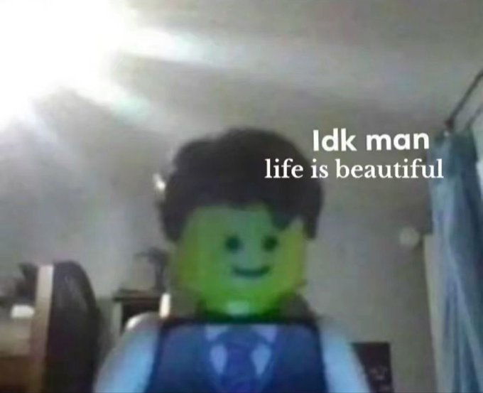 A blurry photo shows a LEGO minifigure with a black hairpiece, smiling face, and blue suit standing in what appears to be a bedroom. White text overlaid on the image reads "Idk man life is beautiful".