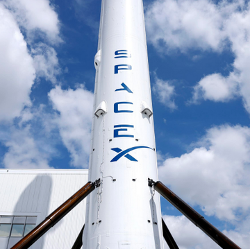 The image features a tall white rocket with blue letters spelling "SpaceX" on its side. The rocket appears to be made of metal, possibly steel, and has two large legs supporting it from below. The rocket is situated against a backdrop of a cloudy sky, which adds an interesting contrast to the industrial nature of the rocket. In the image, there are also some words related to Bitcoin that include " IPO roadshow", "Largest in history", "Buried in the S-1: 18,712 BTC on the balance sheet. Every pension fund, index ETF, and institutional investor that buy SPCX will own Bitcoin whether they want to or not." These words provide context about the rocket's significance and its connection to the world of cryptocurrency.