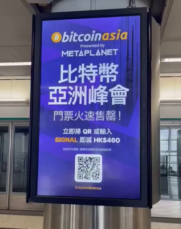 The image features a large billboard with an advertisement for Bitcoin Asia, which was presented at Hong Kong's largest airport. The billboard displays a QR code that can be used to access information about the event or even sign up for it. The text on the billboard is in Chinese and includes details such as the name of the event, the year, and the location. The image also shows a photo of a person holding a sign with Bitcoin written on it. This suggests that there might have been an event related to Bitcoin Asia at the airport where people gathered to learn more about or participate in the event.