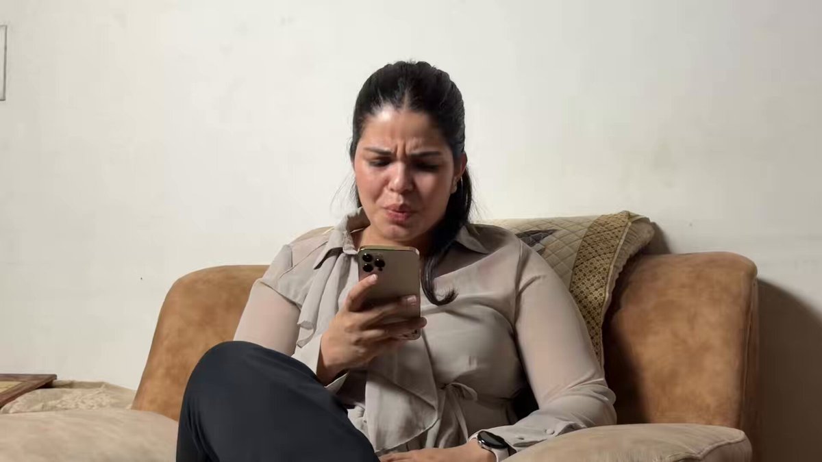 The image shows a woman sitting on a couch, looking at her phone with a concerned expression. She appears to be reading or viewing something on her phone that has caught her attention. The photo also contains text that reads "apple silently delivered: an update that cryptographers thought was IMPOSSIBLE for 40 years: and @fhenix is doing it for our money!". This message seems to be related to the woman's current activity, possibly discussing a recent news article or sharing information with someone else.