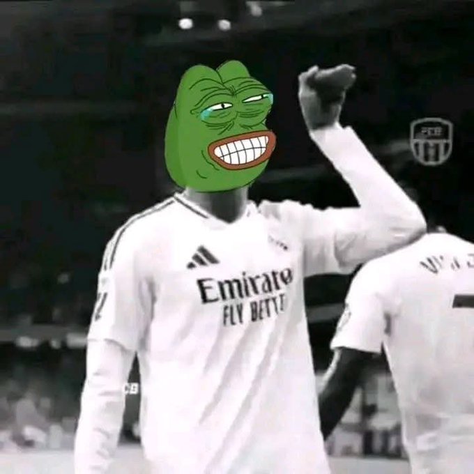 A soccer player in a white Real Madrid jersey with 'Emirate Fly Better' sponsorship and an Adidas logo, with a Pepe the Frog meme face edited over their head, raising a fist.