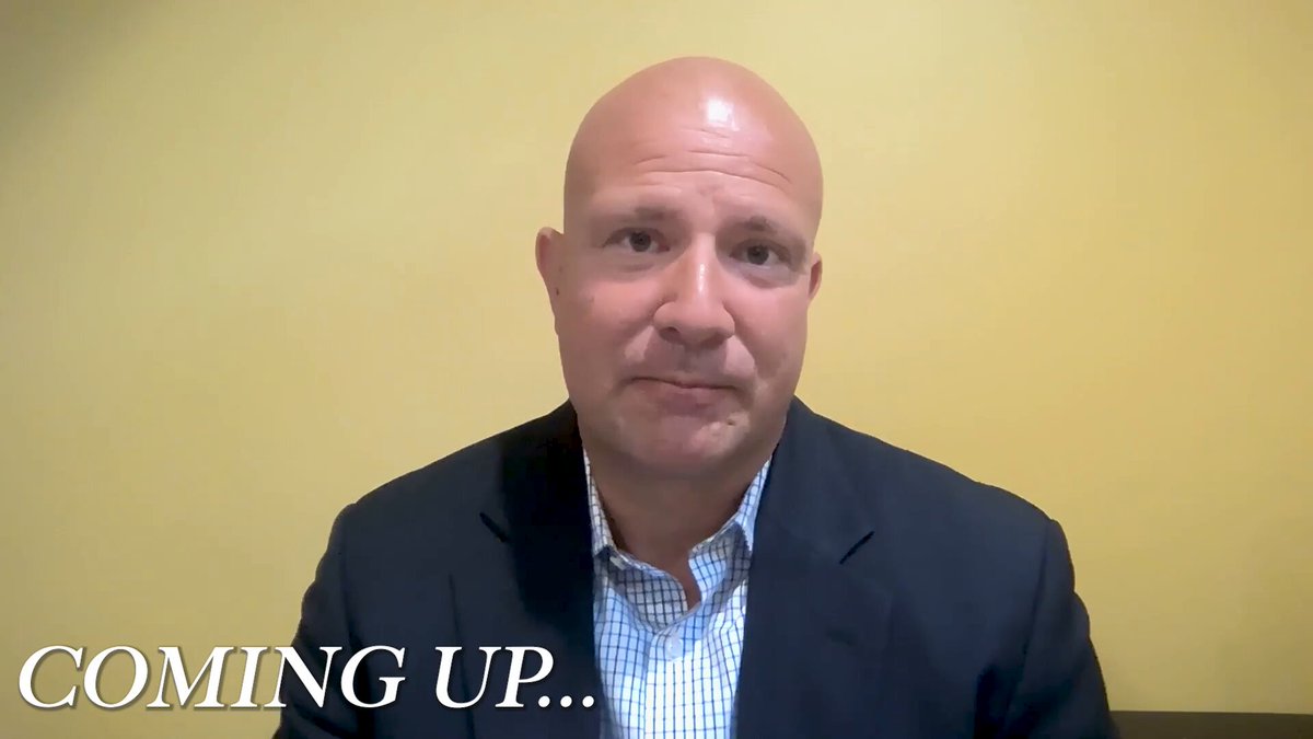 The image features a bald man wearing a suit jacket sitting at a desk with a computer monitor behind him. The background of the image is yellow, which contrasts with the gray wall behind the man. There are two texts displayed in the image that read "coming up... @LukeGromen breaks down his Bitcoin and macro outlook." This suggests that the image might be related to a discussion or analysis about Bitcoin and other financial topics. The man's baldness could also indicate that he is an expert on these subjects, as he appears to be knowledgeable in the field of cryptocurrency and finance.