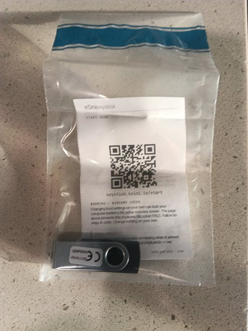 Identical to the previous image, a clear plastic bag holds a black USB drive and a paper insert with a QR code for 'keystick.io'.