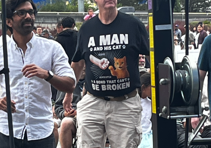 A man proudly wears a graphic t-shirt reading "A MAN AND HIS CAT: BOND THAT CAN'T BE BROKEN," featuring an illustration of an orange cat doing the "boop" gesture with a fist. The post's caption about wanting to be "old and cool" playfully reflects the man's confident, cat-loving vibe captured in the photo.