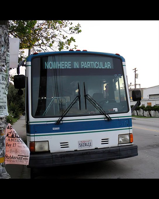 A blue and white Gillig transit bus parked on a street displays the destination sign 'NOWHERE IN PARTICULAR' and has a California license plate reading '5XZA611'.
