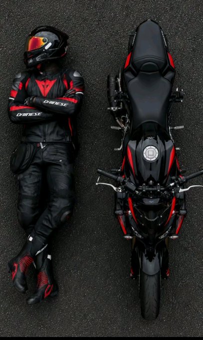 A top-down view of a motorcyclist in black and red Dainese gear lying next to a black and red sportbike on asphalt.
