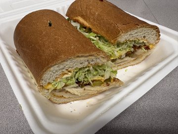 Two halves of a sandwich with lettuce and meat fillings on a brown bread roll, served in a white takeout container.