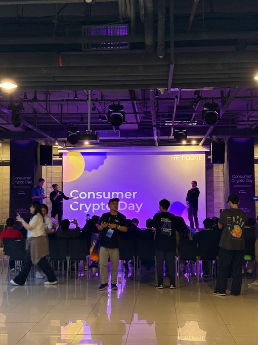 A conference event titled 'Consumer Crypto Day' hosted by Fluent is shown, with attendees gathered in front of a stage featuring a large screen displaying the event name.