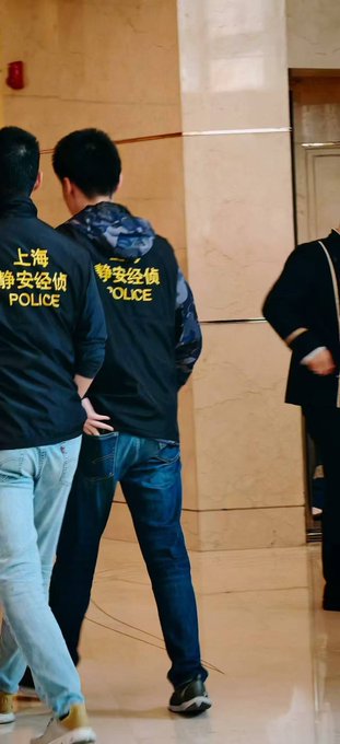 The image shows several individuals wearing police vests labeled "POLICE" and Chinese characters "上海静安经侦" (Shanghai Jing'an Economic Crime Investigation), standing in what appears to be a lobby with marble walls. This visually supports the post's reference to being taken to a police station in Shenzhen by economic crime investigators, illustrating the "offline" consequences the poster describes following their online complaints about Solana's aggressive token launch practices.