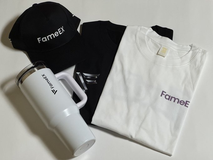 FameEX branded merchandise including a black cap, white and black t-shirts, and a white travel tumbler/mug arranged on a white surface.