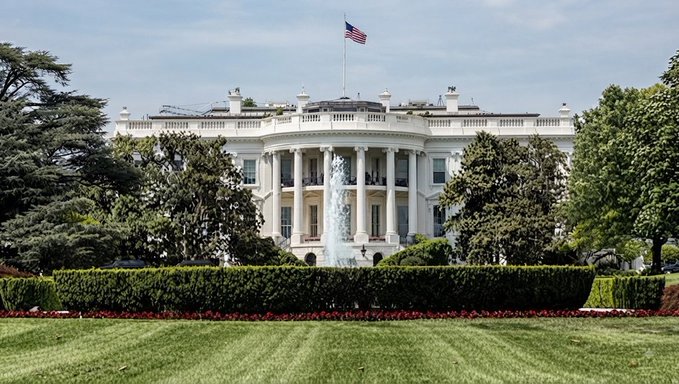 The White House stands prominently with the American flag flying atop, its iconic columned facade and south lawn fountain in full view. The image underscores the gravity of the post's news that Ripple executives are heading to the White House today for a high-stakes meeting with President Trump, the SEC, CFTC, and other major crypto leaders to discuss the CLARITY Act and the future of digital asset regulation in America.