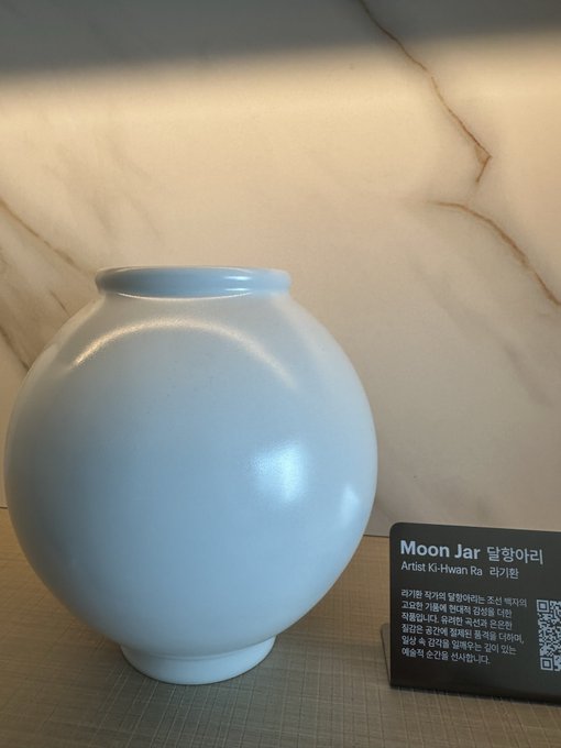 A pale blue ceramic Moon Jar (달항아리) by artist Ki-Hwan Ra (라기환) sits on a woven mat against a marbled backdrop, displayed with a Korean-English placard describing the traditional Korean pottery style. The caption "First thing I see is this:" captures the poster's immediate impression upon arriving in Korea for KBW (Korea Blockchain Week), where this elegant vessel greeted them.