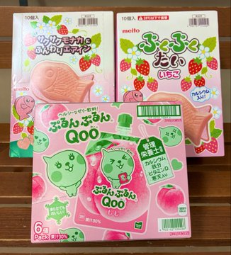 The image features three boxes of pink food items, each with a different flavor or type of food inside. The first box contains a fish-shaped treat, while the second one has a strawberry-flavored item. The third box also holds a strawberry-flavored item. These boxes are placed on top of a wooden surface, and there is text visible in the image that reads "今日も今日とて、会社帰りとて #STEPN と クレーンゲーム 1,800円で色々な台を遊んで、最終的に三つのお菓子を獲得 ズリげる". The image is related to a post about the different flavors of pink food items, and it appears that there are three boxes in total.