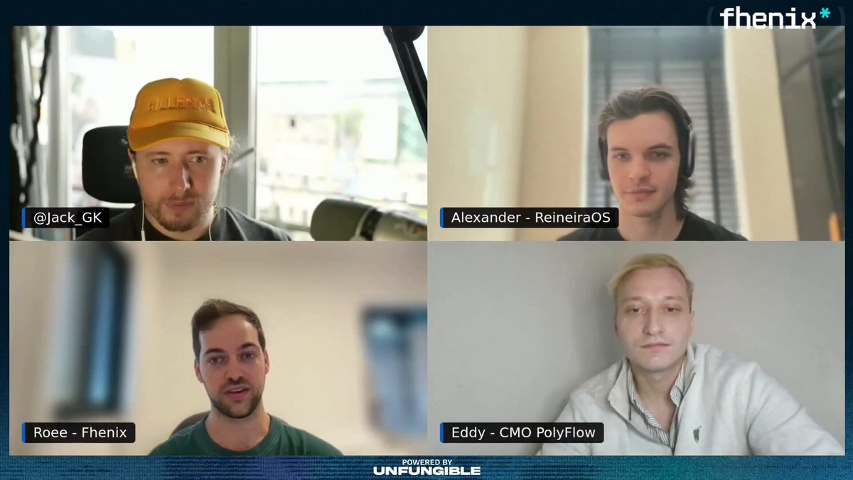 The image shows four men sitting behind computer screens with their faces displayed on them, likely participating in a video conference call or meeting. The background of the image features a window that allows natural light into the room. One man has his face partially visible while looking at the camera, and another is wearing headphones. The other three men are also looking at the camera, indicating they are engaged in the conversation.