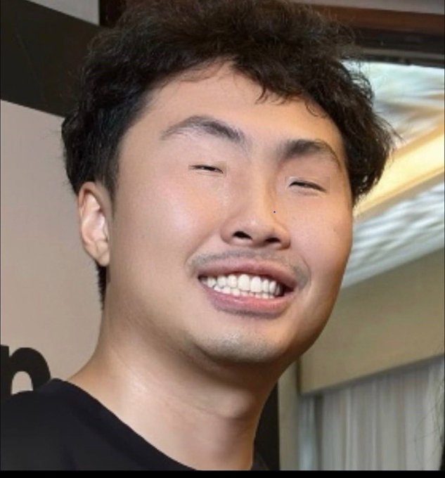 A close-up selfie of a smiling East Asian man with curly dark hair wearing a black shirt.