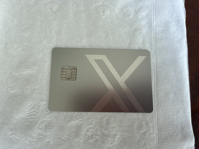 A metallic credit card with a chip and a large 'X' design lies on a white paper towel with a shell pattern.