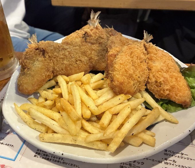 The image shows a plate of food consisting of fried chicken, french fries, and salad greens. The plate is placed on top of a dining table with a person partially visible behind it. The photo has been captioned with Japanese text that reads "久しぶりのアジフライ部に参戦！ スタート".
