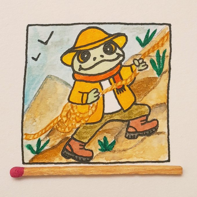 A watercolor and ink illustration shows a frog character dressed in an orange outfit and hat, holding a rope, mounted on paper with a wooden matchstick placed below it.