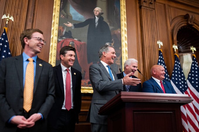 Republican congressional leaders, including Paul Ryan, Kevin McCarthy, Speaker John Boehner, Senate Majority Whip John Cornyn, and Majority Leader Mitch McConnell, share a laugh at a podium bearing the Trump name during a press conference, seemingly celebrating a legislative victory the day before a key vote on the "Clarity" bill.