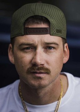 A man wearing a green cap and gold chain looks at the camera with a serious expression.

The image appears to be a portrait of country music singer Morgan Wallen, whose serious pose and styling complement the post projecting him to become Billboard's #1 top artist of 2026 according to Polymarket traders.