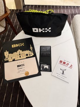 An OKX branded bag, an 'ARKAD' book, and other items resting on a white table.