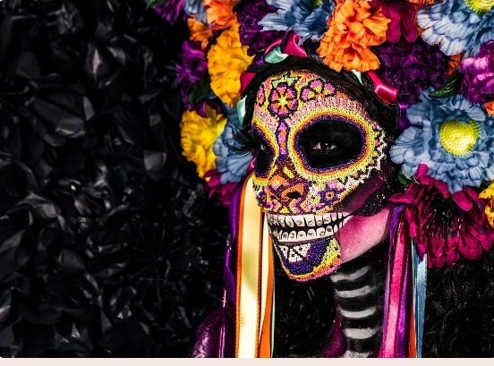 urn of flowers with purple, yellow, and orange petals is placed on a black background, accompanied by a woman's face painted in pink, blue, green, and purple colors.