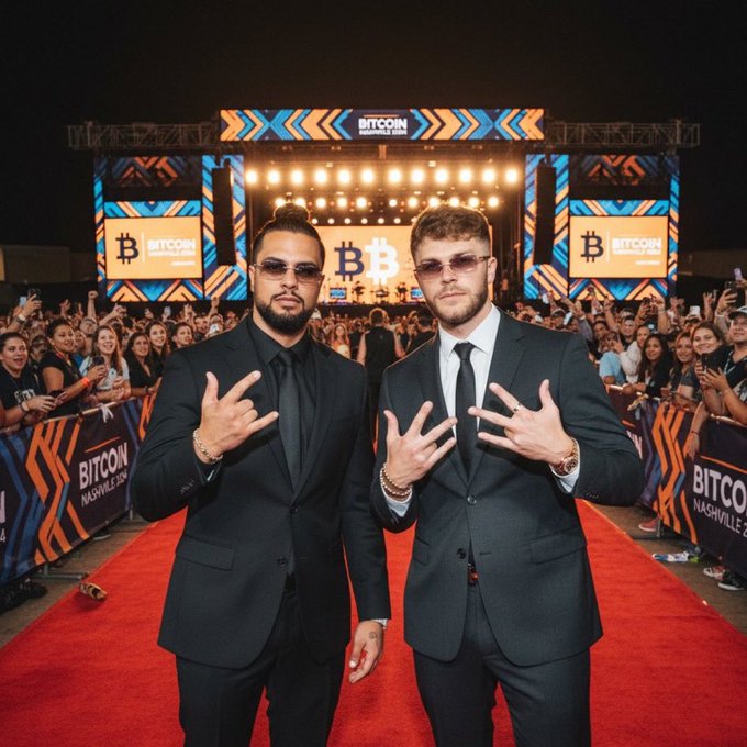 Two men in dark suits and sunglasses pose on a red carpet at the Bitcoin 2024 Nashville conference, with Bitcoin logos and signage visible on the stage behind them.