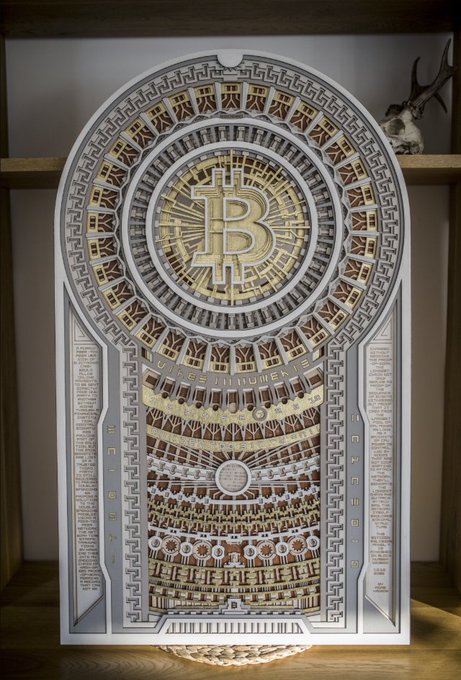 An ornate, intricately designed Bitcoin (BTC) themed decorative art piece featuring the ₿ symbol in a circular mandala-like structure with gold and silver detailing, displayed on a wooden shelf.