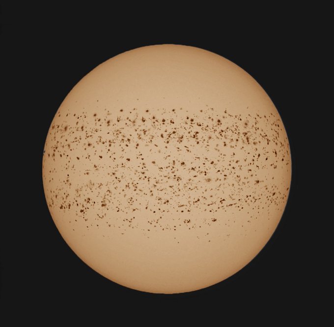 A 3D rendered illustration of a peach or light orange colored planet/sphere with brown speckled patterns across its middle, set against a black background.