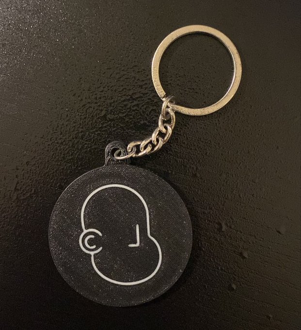The image features a black and white keychain with a cartoon-like face design, likely representing an NPC (Non-player character). The keychain has a silver ring attached to it, which could be used for opening doors or interacting with other characters in the game. The post suggests that this keychain is designed specifically for players who want to personalize their gaming experience by attaching it to their in-game items and using it as a unique identifier within the gaming community.