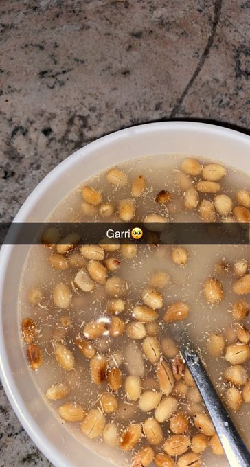 A bowl of what appears to be a grain or legume dish floating in liquid, labeled 'Garri' with a smiling face emoji overlay, with a spoon visible in the bowl.