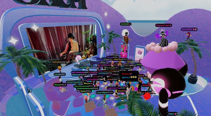 A screenshot from a vibrant virtual world shows a DJ performing on a stage decorated with palm trees, clouds, and pink/purple decor for a "SheFi Graduation Party" celebrating Cohort 17, with numerous avatar usernames like "SJCDIA," "PrincessTrash," and "DannyDCL" floating throughout the scene as attendees gather for the crypto and metaverse celebration.